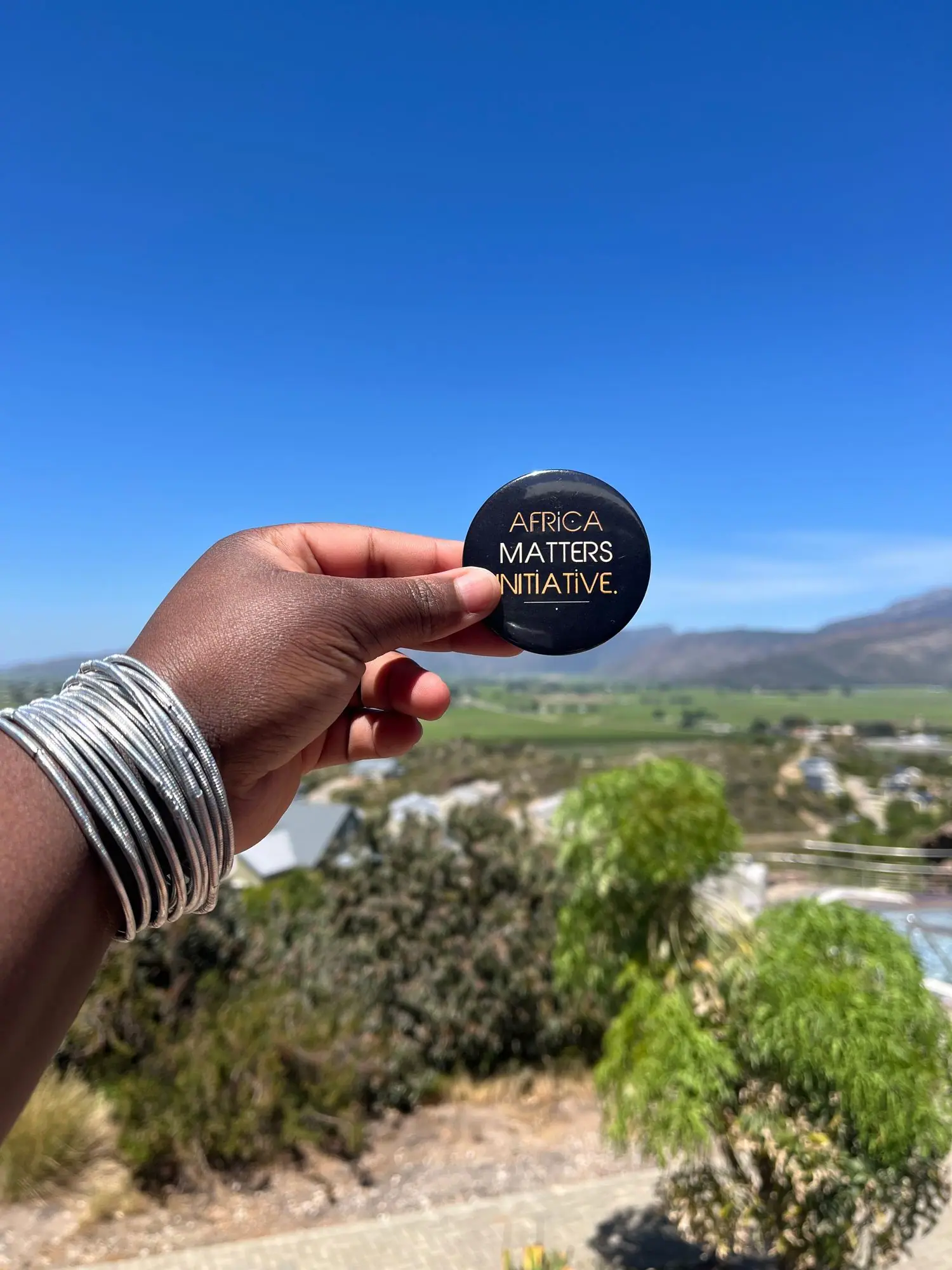 Hand holding an Africa Matters badge against a mountain view