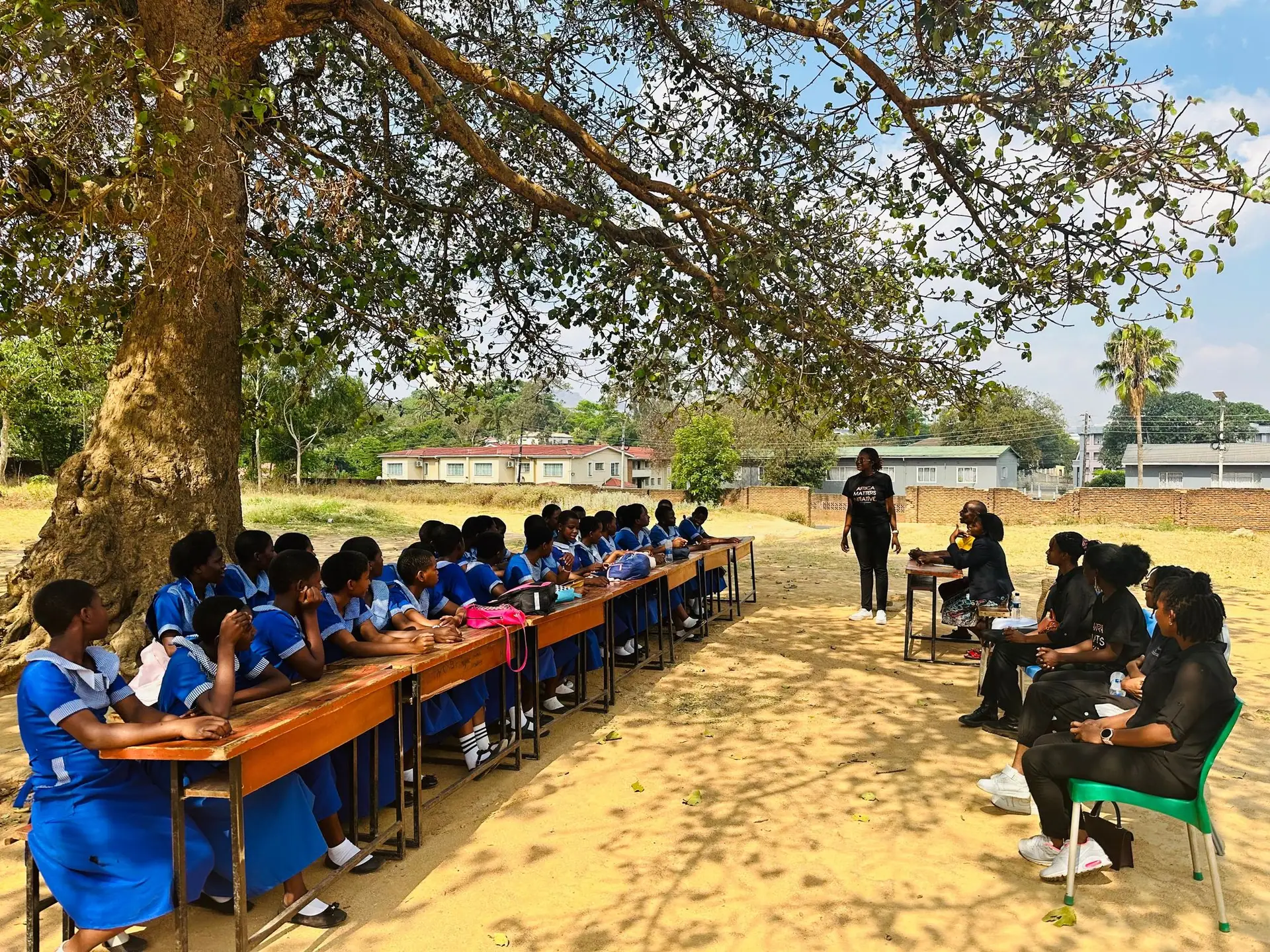Learners at desks for an outdoor class under a tree