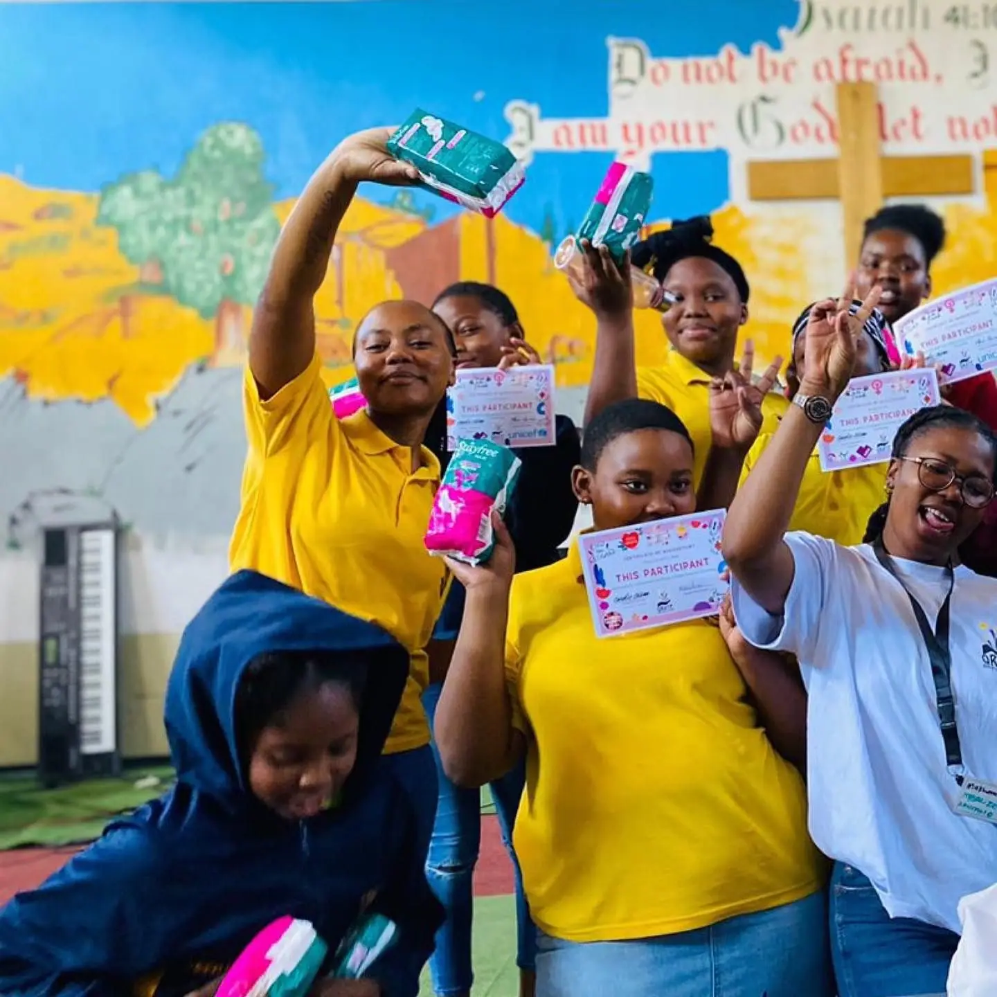 Learners in yellow shirts celebrating with menstrual health kits