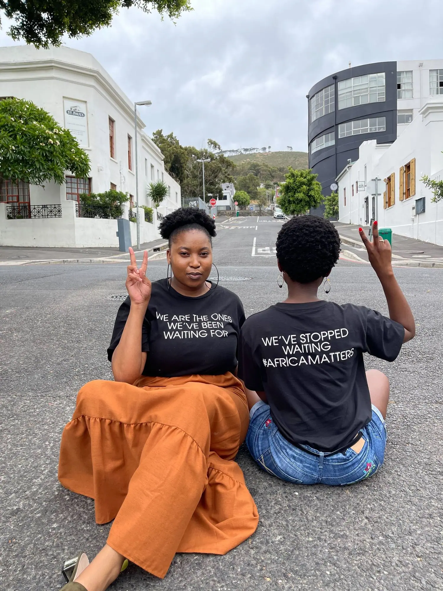 Two young women in We've stopped waiting T-shirts sitting on a street